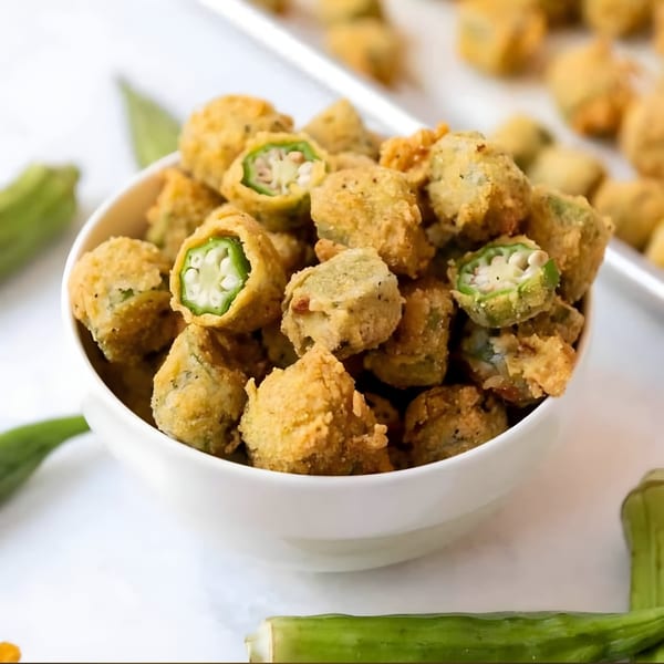 A white bowl filled with crispy, golden-brown fried okra, some showing their green interior.