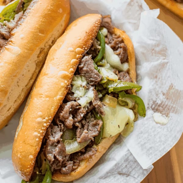 Two R Burger N Wings cheesesteak sandwiches with steak, onions, and green peppers on a bun.