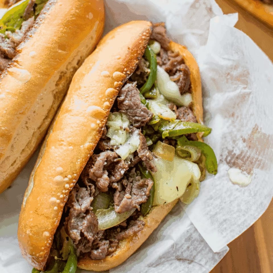 Two R Burger N Wings cheesesteak sandwiches with steak, onions, and green peppers on a bun.