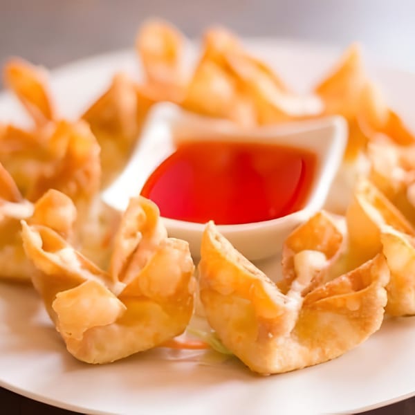 Crispy crab rangoon appetizers with sweet and sour dipping sauce on a white plate.