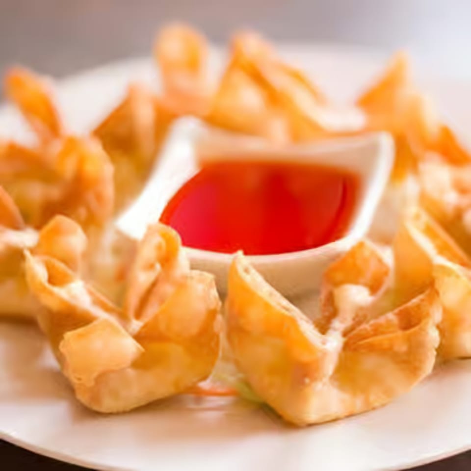 Crispy fried wontons arranged around a small white bowl of bright red dipping sauce.